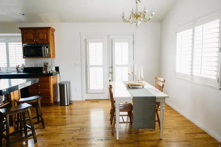 Kitchen and dining area featuring hardwood flooring, white plantation shutters, a white dining table with wood chairs, a kitchen island with dark countertops, and wood cabinetry