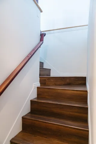 Staircase featuring wood-finish treads and risers, white painted walls, and a contrasting wood handrail