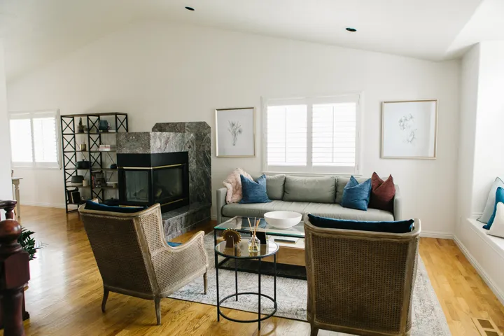 Spacious living area featuring a fireplace with surround, vaulted ceiling, wood flooring, and multiple windows with plantation shutters
