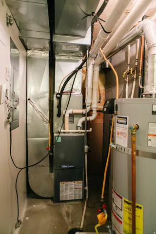 Utility area featuring an American Standard furnace, a water heater, extensive ductwork, and exposed piping