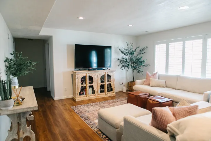 Spacious living area featuring wood-finish flooring, recessed lighting, and a large window with plantation shutters