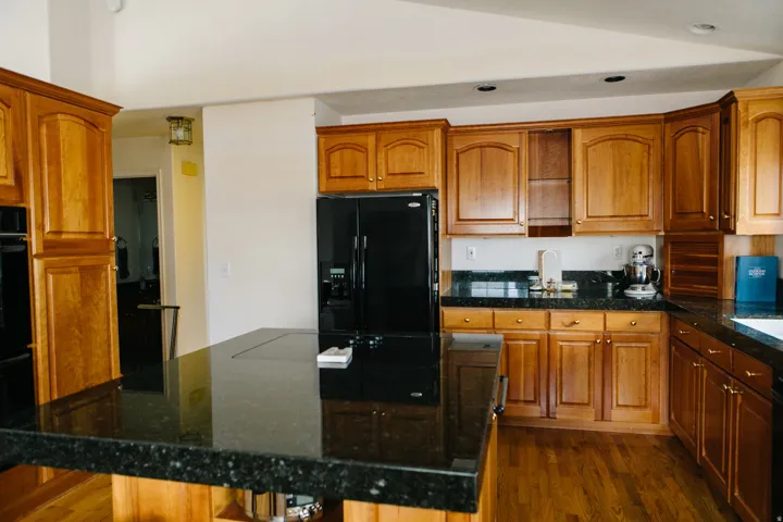 Kitchen featuring wood cabinetry, dark granite countertops, black appliances