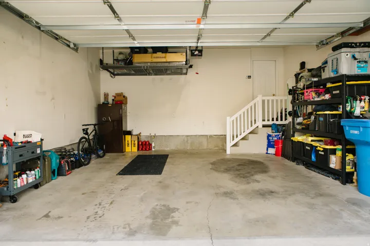 Spacious garage featuring a concrete floor, overhead storage rack, and a staircase with a white railing