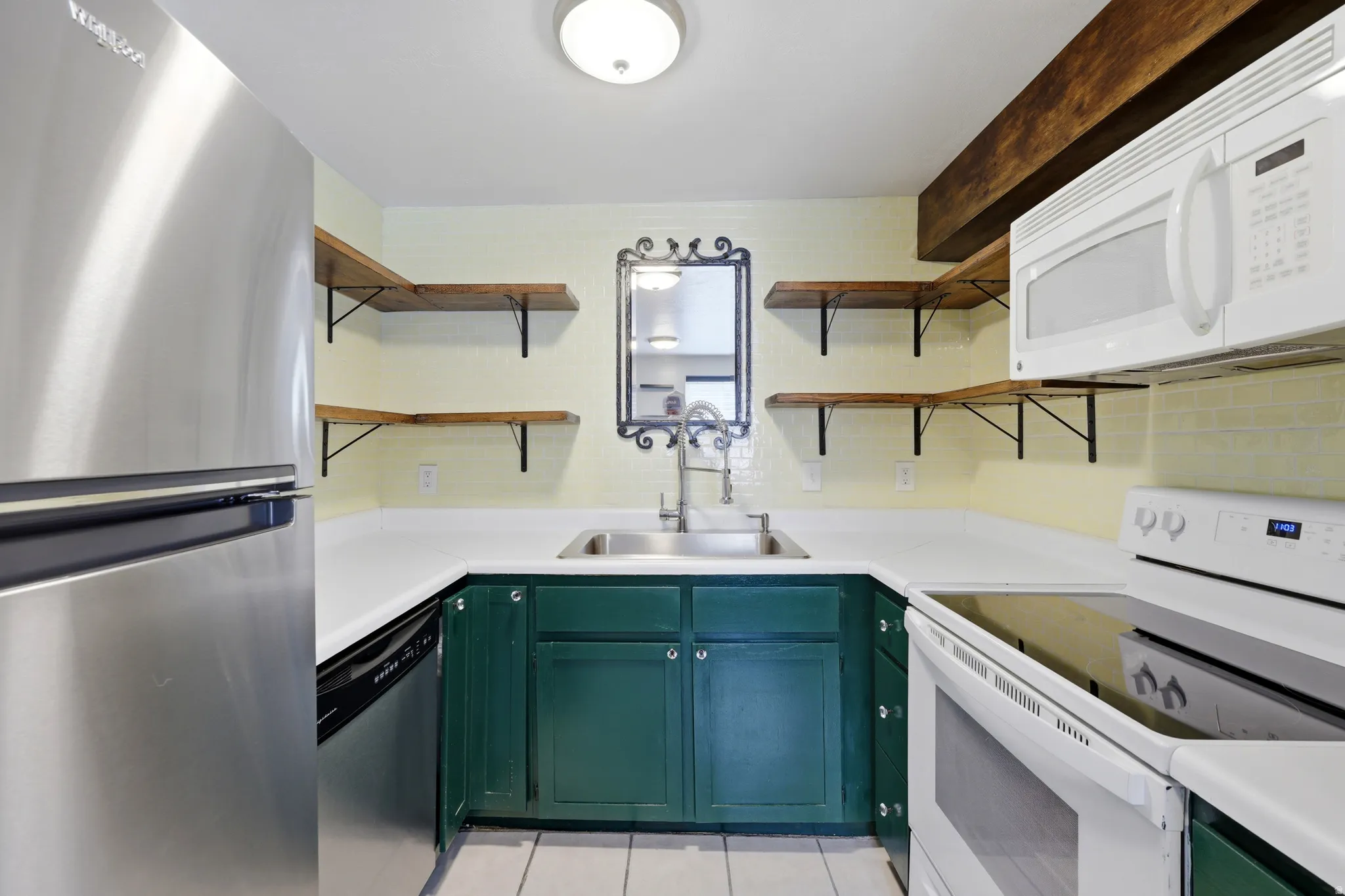 U-shaped kitchen with green cabinetry, white countertops, a stainless steel refrigerator, and open wood shelving