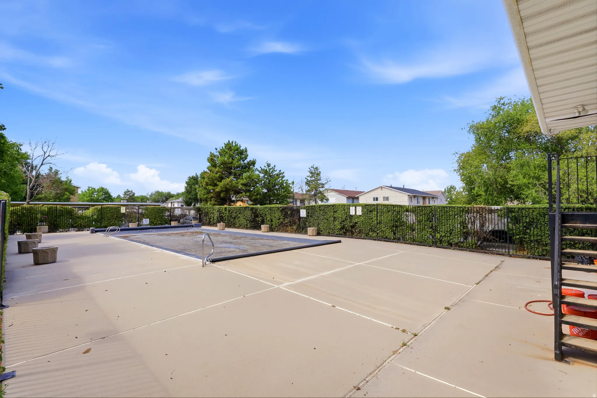 Outdoor swimming pool with a protective cover, surrounded by a concrete deck and a black metal fence