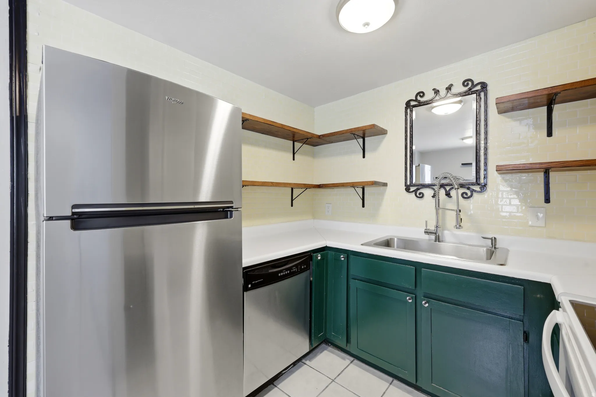 Kitchen featuring a stainless steel refrigerator, dark green base cabinetry, white countertops, and open wood shelving