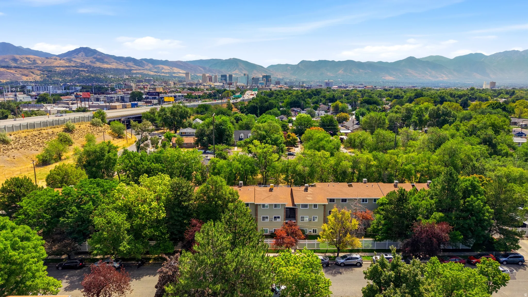 Residential buildings set amongst mature trees, with a distant city skyline and mountain backdrop