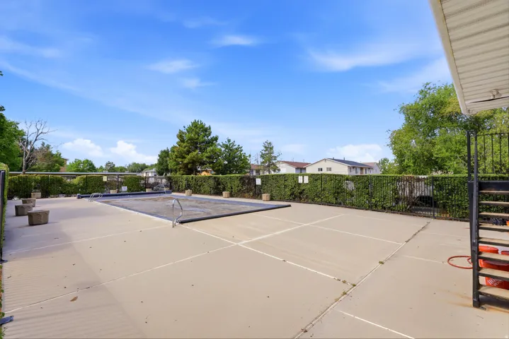 Outdoor swimming pool with a protective cover, surrounded by a concrete deck and a black metal fence