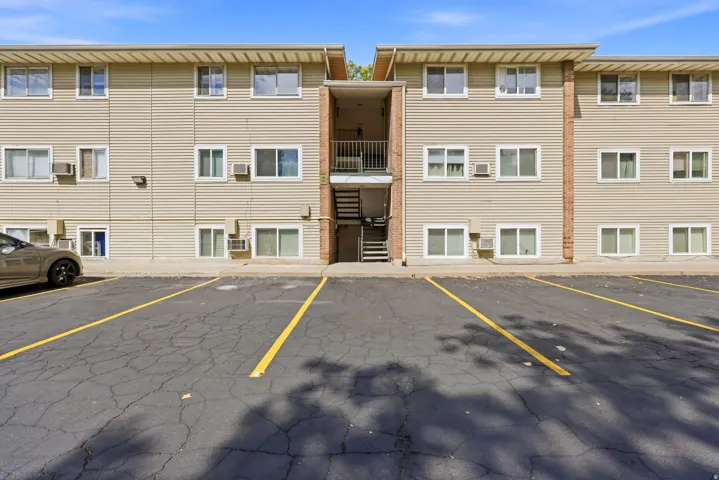 Multi-level building with horizontal siding and multiple windows, featuring an exterior stairwell and a paved parking area with yellow striping