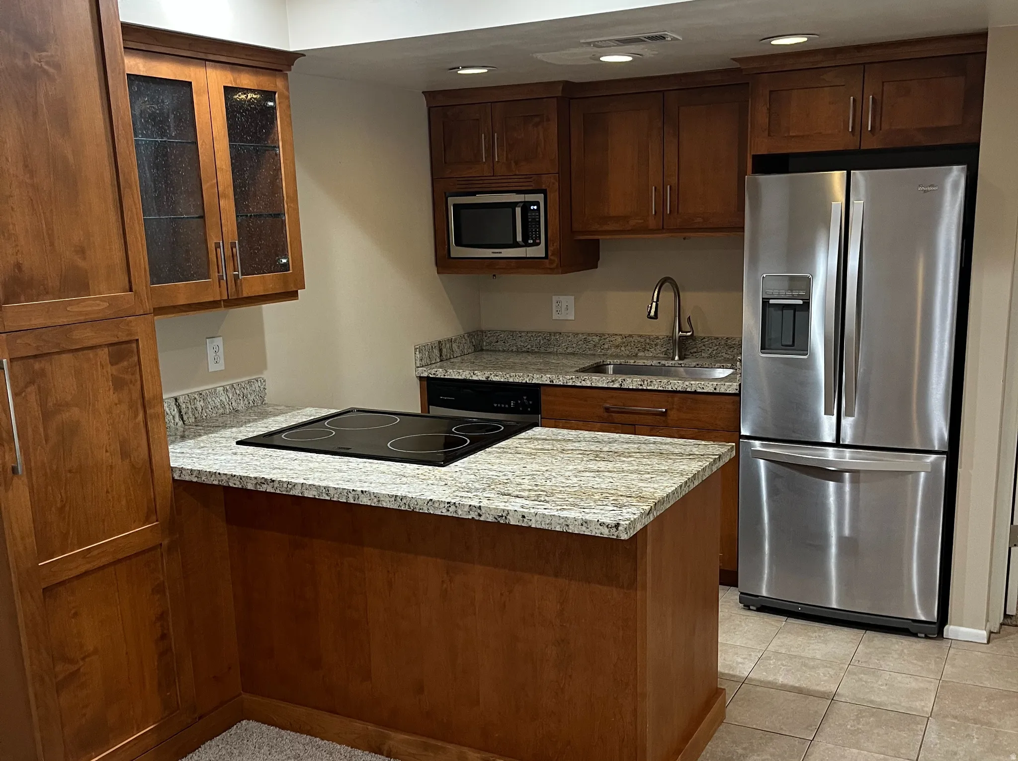 Kitchen featuring wood cabinetry, granite countertops, stainless steel appliances, and an electric cooktop