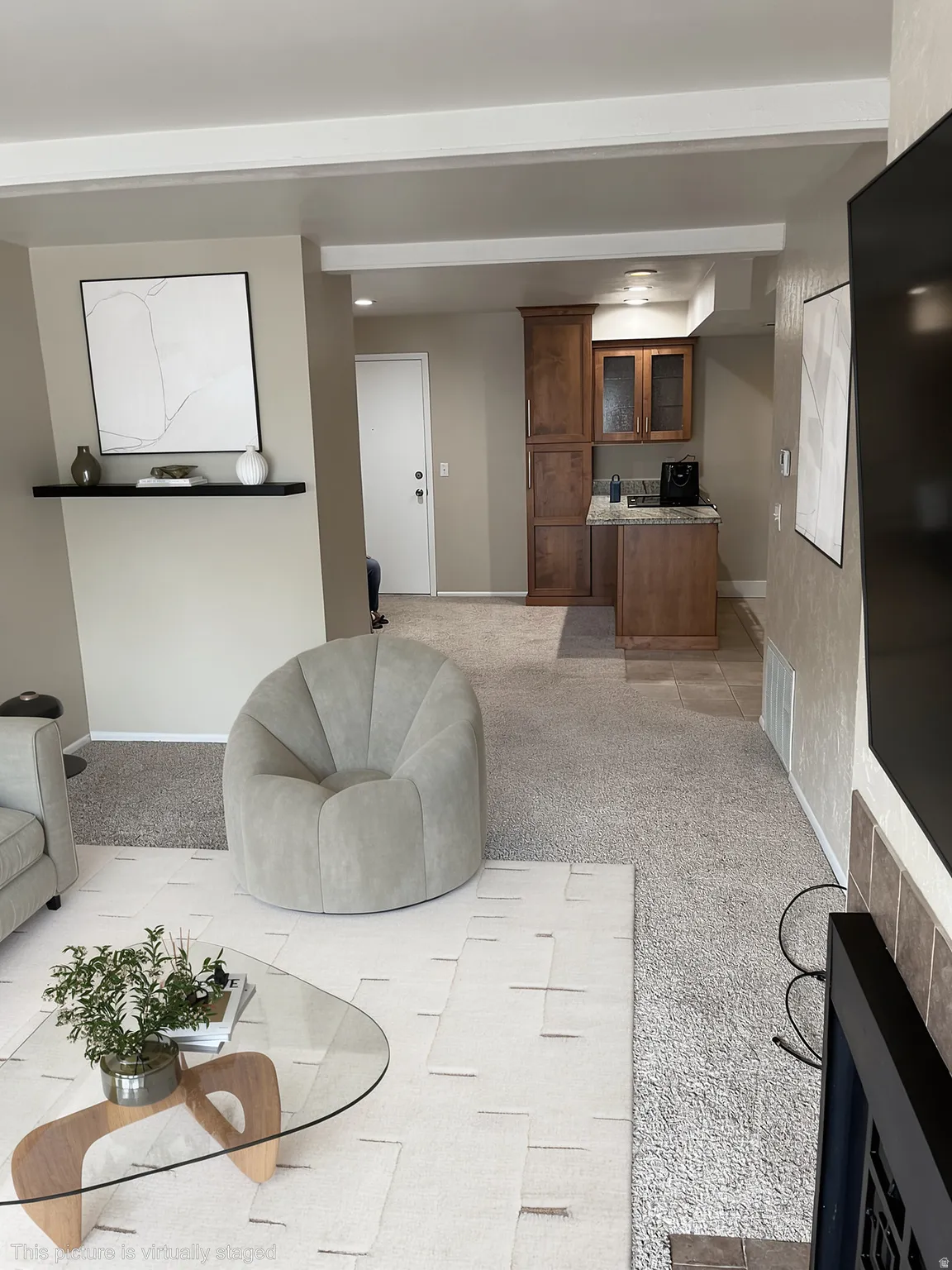 Built-in shelving unit, compact kitchen area with wooden cabinetry, integrated lighting, and carpeted flooring