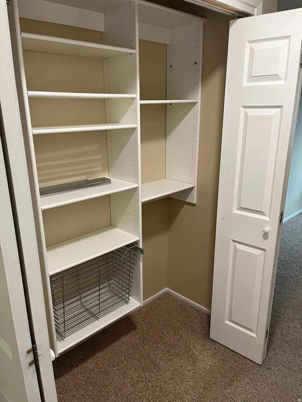 Built-in closet organization system featuring adjustable white shelving and a wire pull-out basket