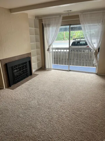 Living area featuring a sliding glass door to an exterior balcony, built-in shelving, a fireplace with a dark metal insert, and neutral-toned carpeting