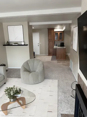Built-in shelving unit, compact kitchen area with wooden cabinetry, integrated lighting, and carpeted flooring