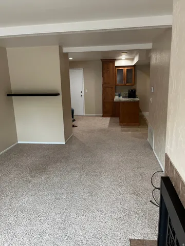 Neutral-toned carpeting, recessed lighting, wood-finish cabinetry with glass-front accents, tiled flooring in the kitchen area, and a tiled fireplace surround
