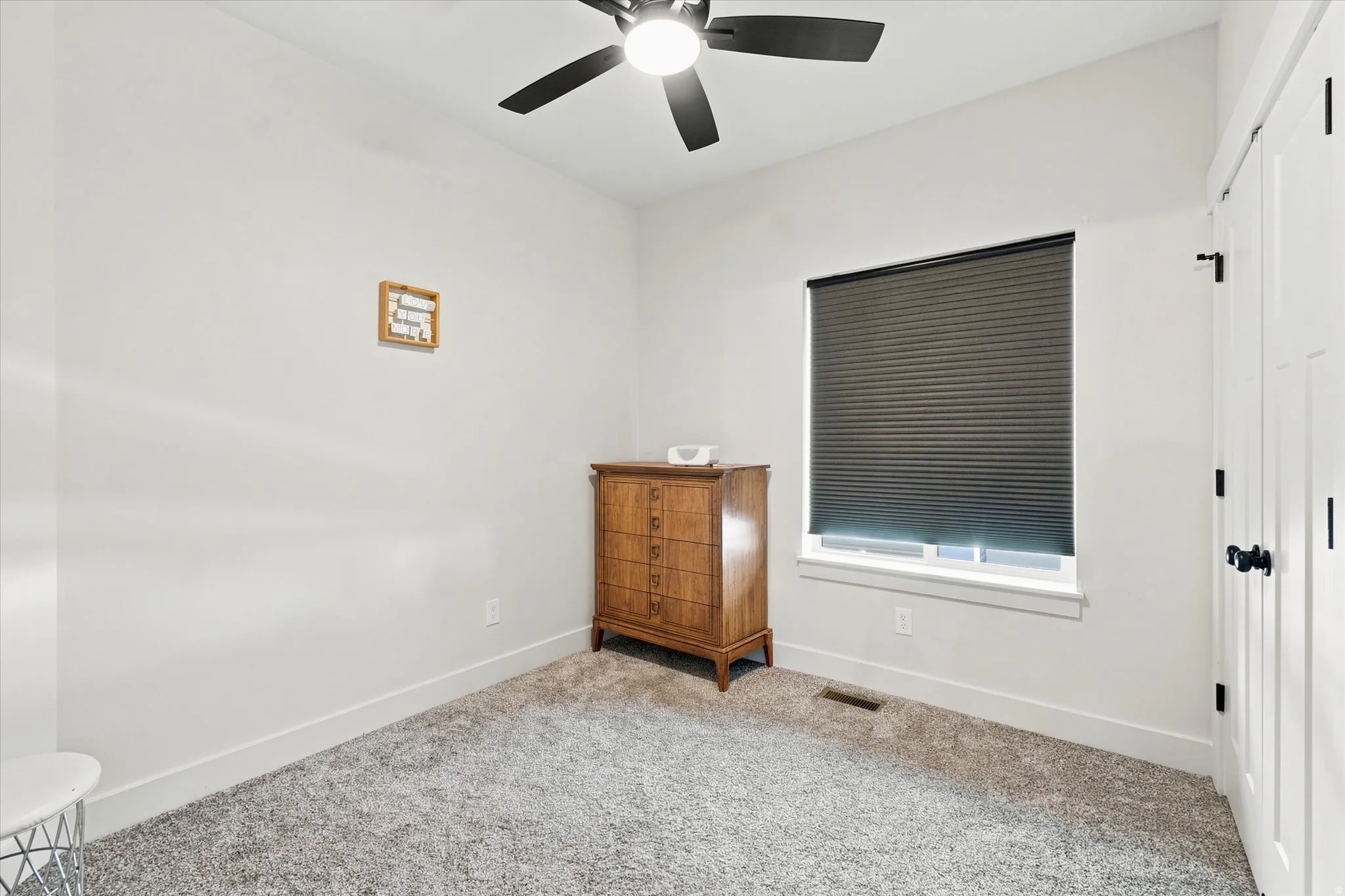 Bright room featuring a window with cellular shades, a ceiling fan with black blades, and light gray carpet flooring