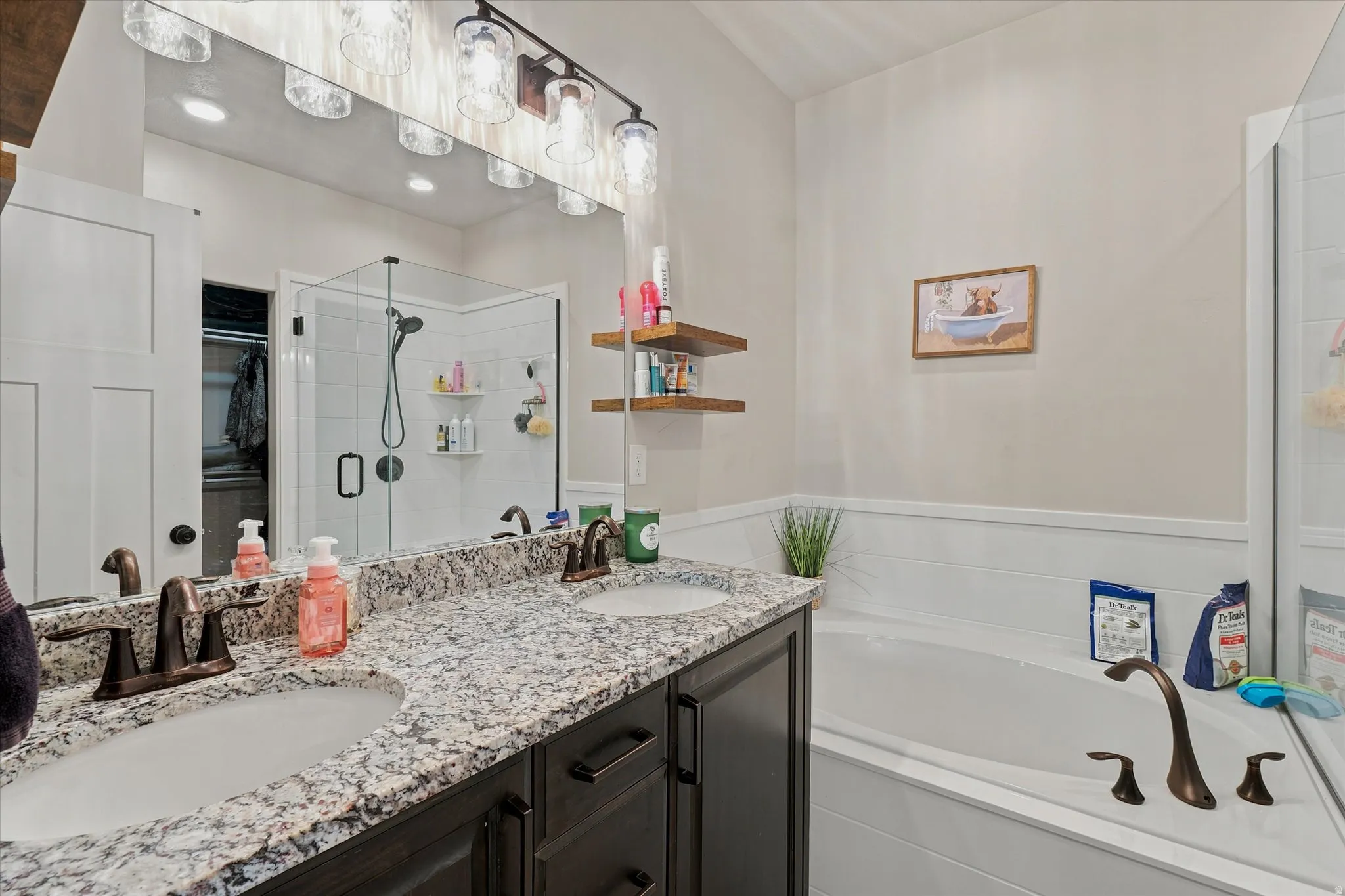 Bathroom featuring a dual vanity with granite countertop, bronze-finish fixtures, and a corner soaking tub