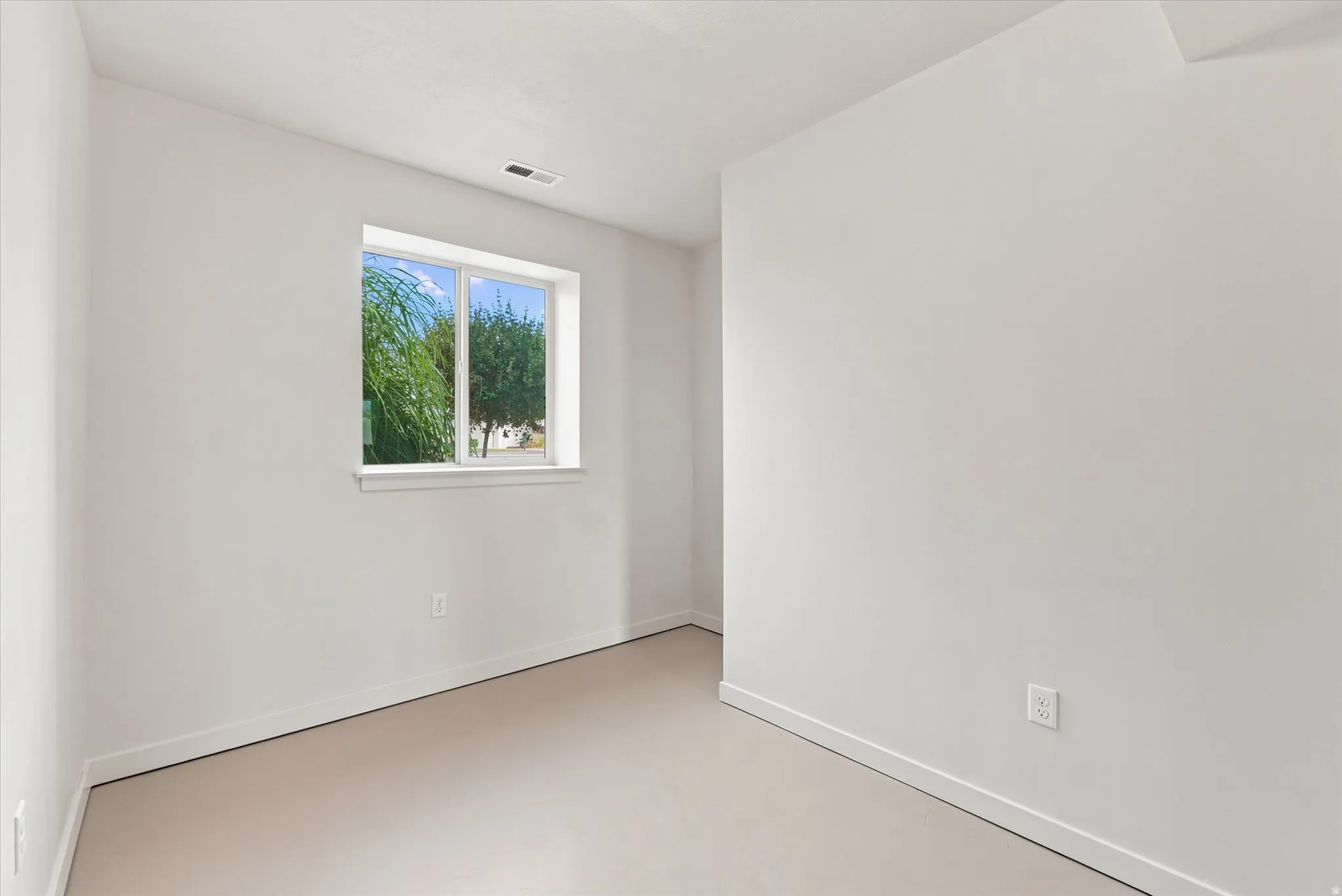 Bright interior space with a window offering exterior views, light-toned flooring, white walls, and a white baseboard trim