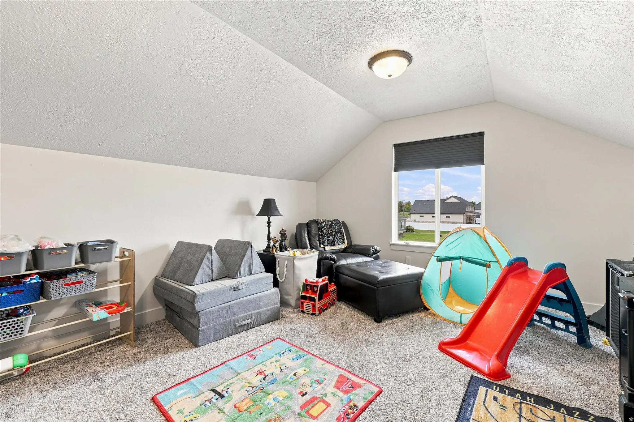 Carpeted room with a vaulted ceiling and a single window featuring a dark blind