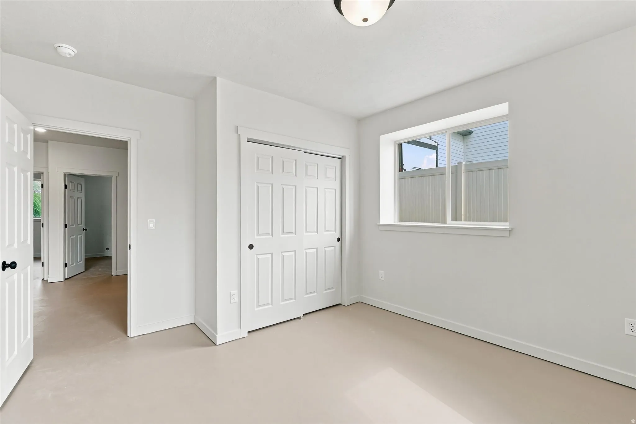 Bedroom featuring neutral carpeting, a large window, a ceiling light fixture, a closet with bifold doors, and white trim