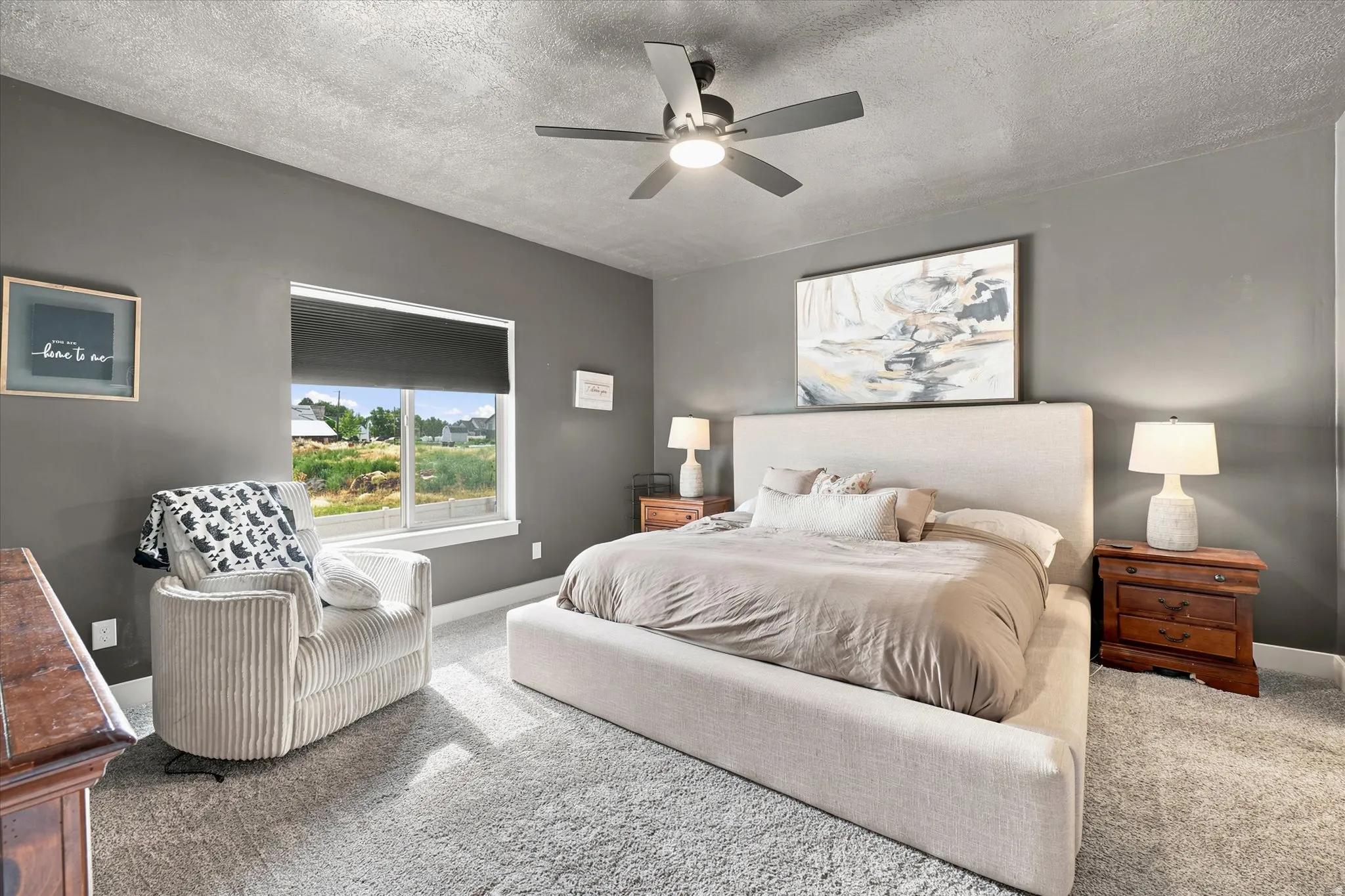 Spacious bedroom featuring neutral carpeting, a ceiling fan with integrated lighting, and a window with a roller shade