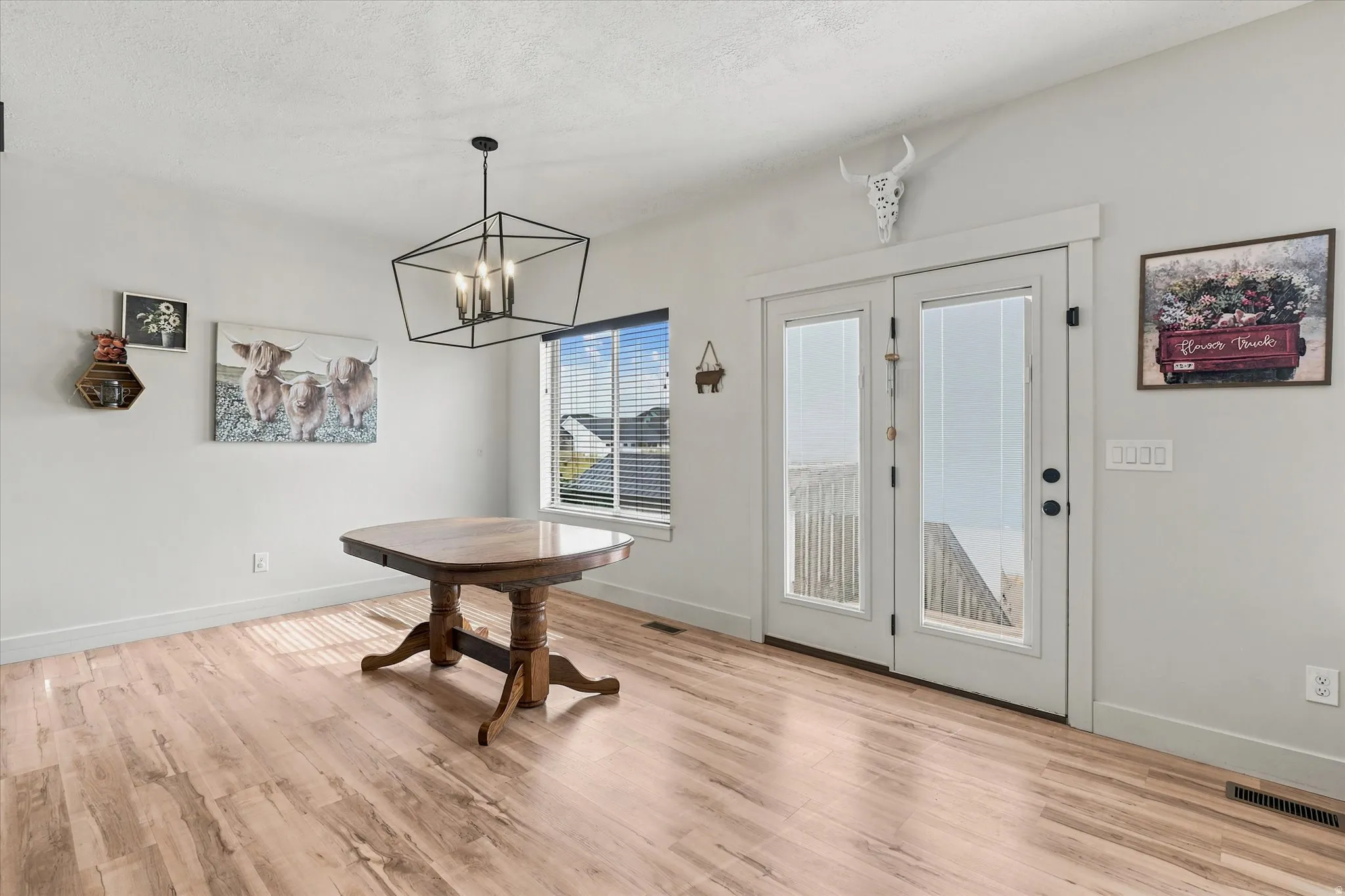 Spacious room featuring wood-finish flooring, a contemporary geometric chandelier, and white walls
