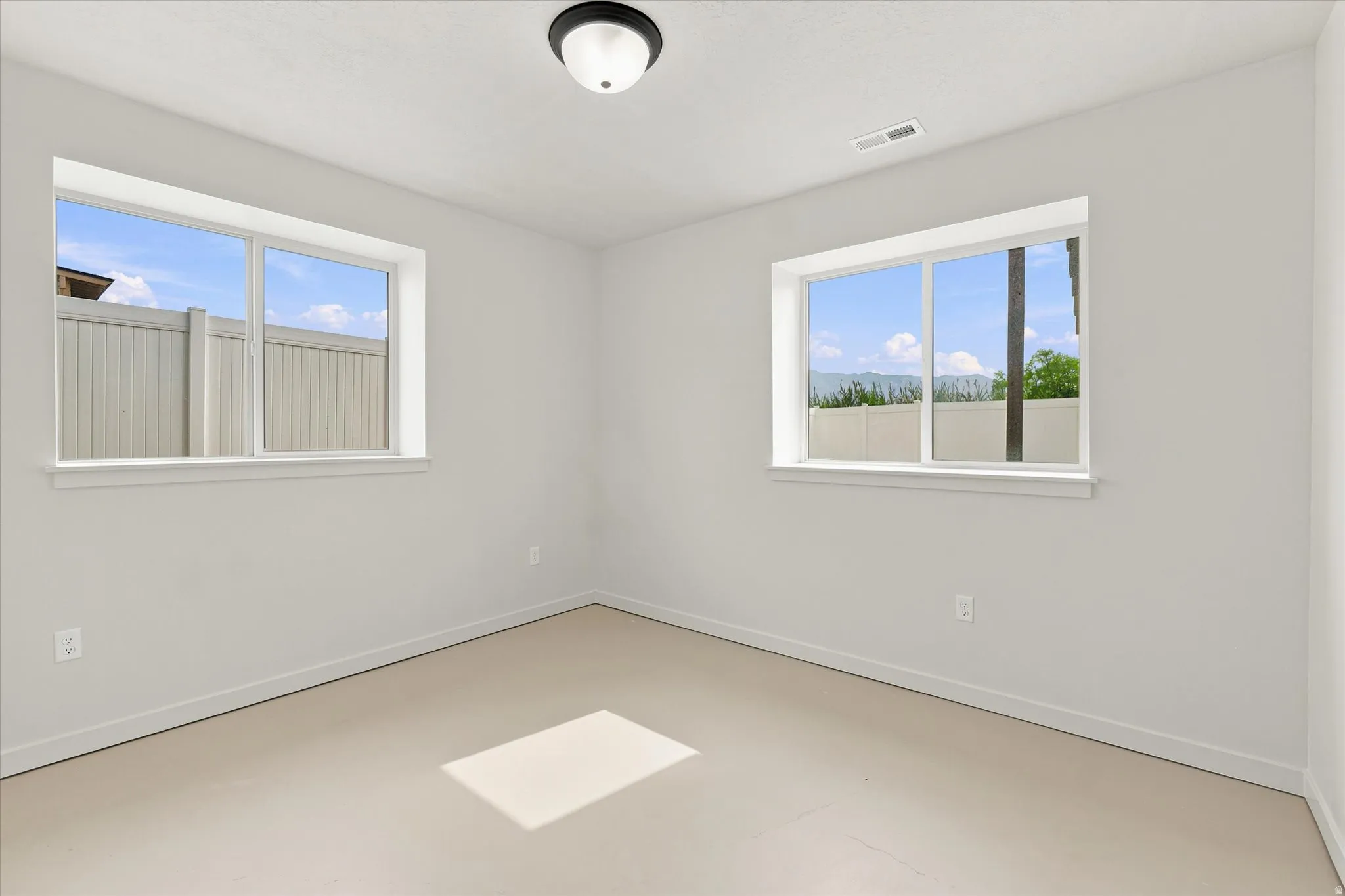 Bright interior room featuring neutral wall paint, two large windows, white trim, and light-colored flooring