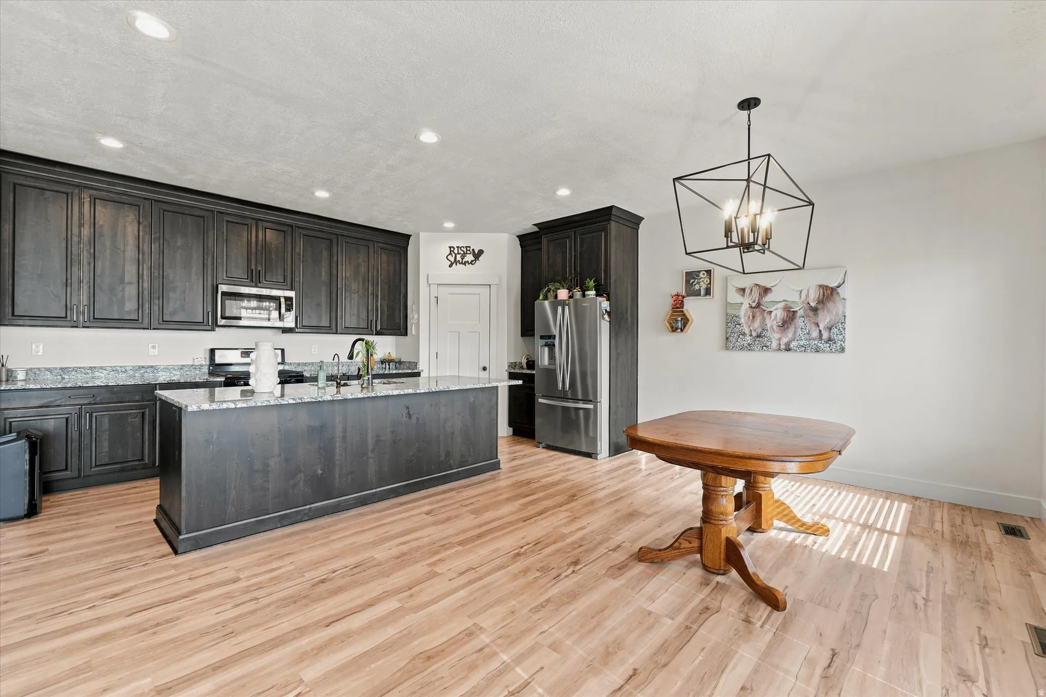 Spacious kitchen featuring dark wood cabinetry, granite countertops, a large center island, wood-finish flooring, and a contemporary geometric chandelier