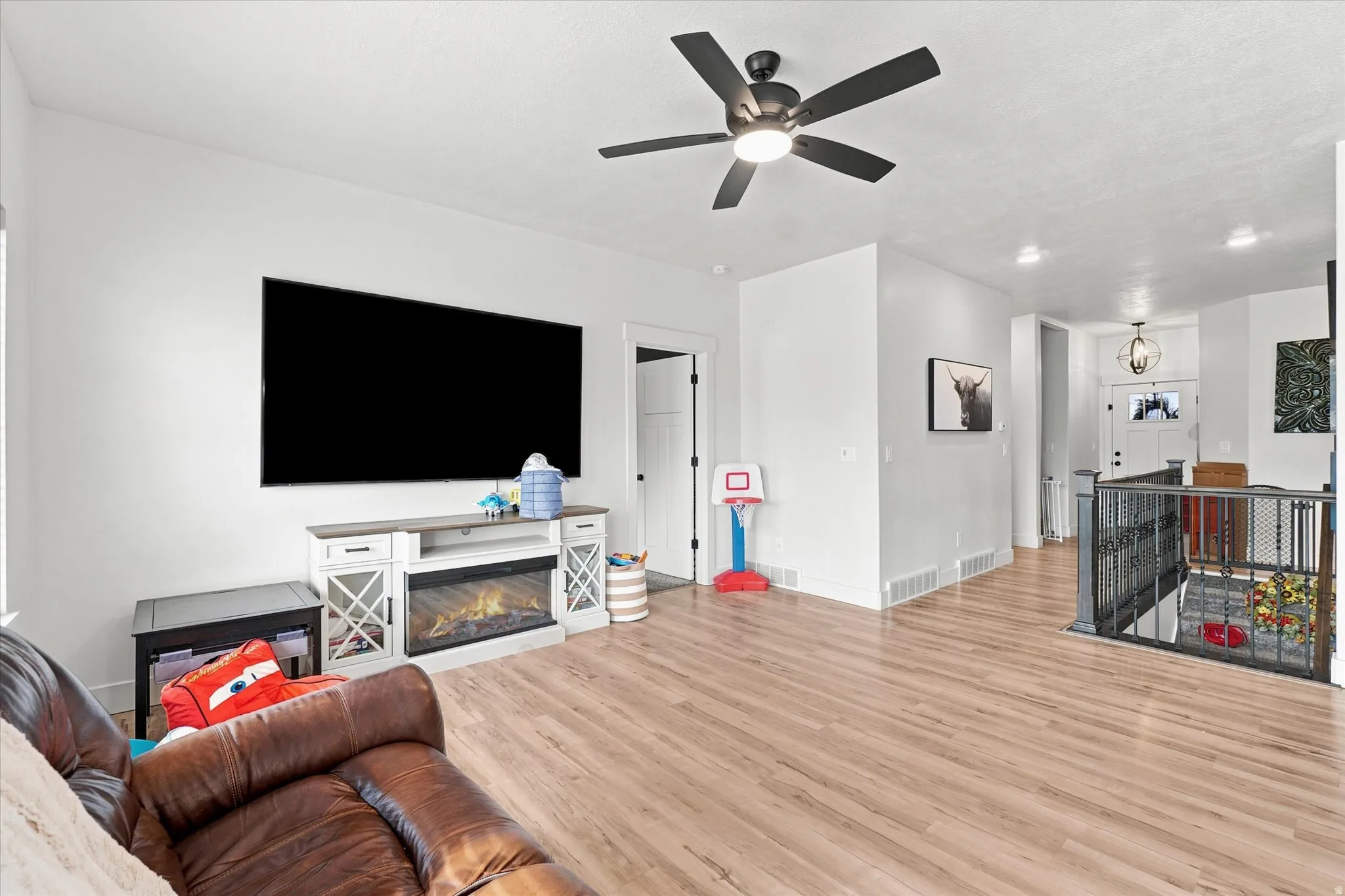 Spacious living area featuring wood-finish flooring, a ceiling fan with integrated lighting, and a media console with an electric fireplace