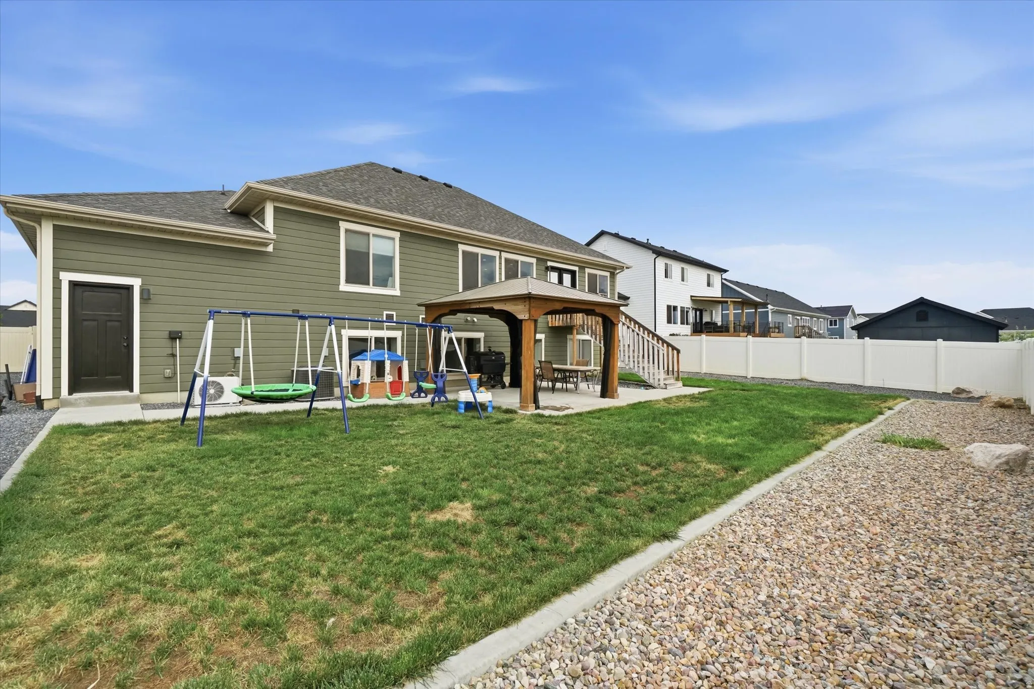 Expansive backyard featuring a green lawn, a dedicated gravel area, a private patio with a gazebo, and a full privacy fence