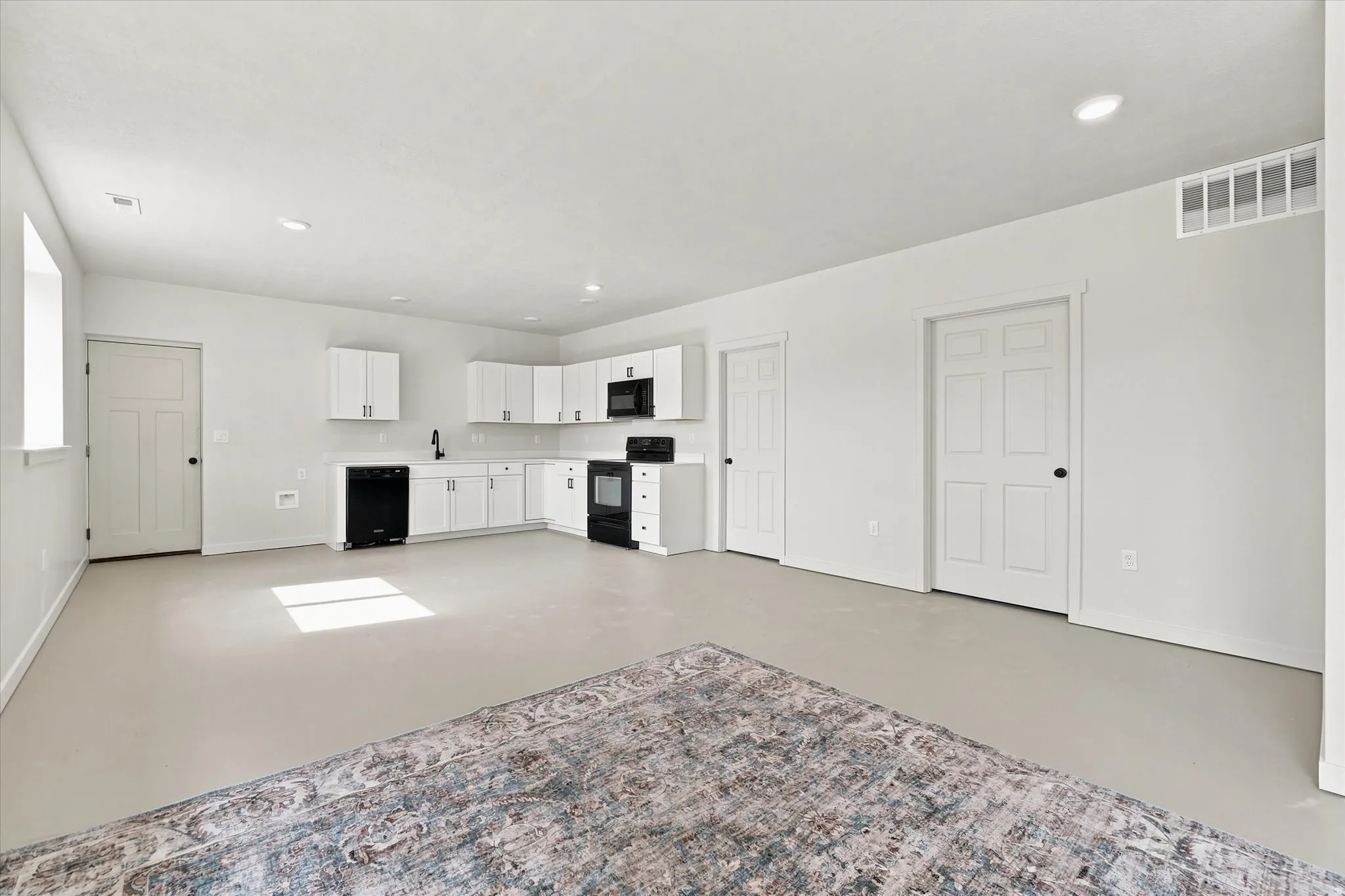 Open-concept kitchen with white cabinetry and black appliances, recessed lighting, and light-toned flooring