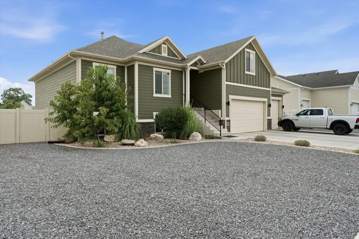 Contemporary residence featuring a two-car garage, gravel parking area, and a light-colored privacy fence