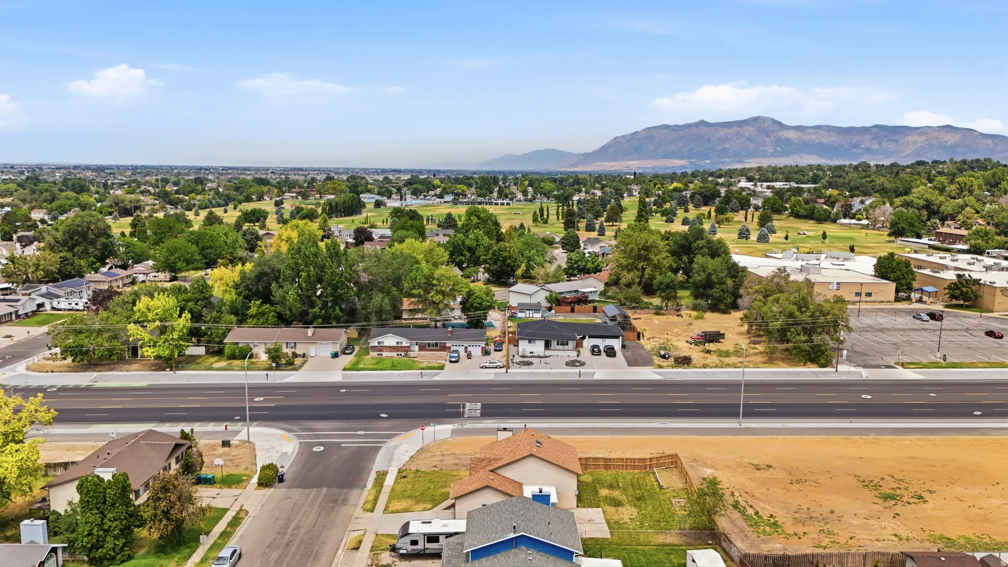 Expansive aerial perspective showcasing a neighborhood with mature trees, a wide paved road, and distant mountains