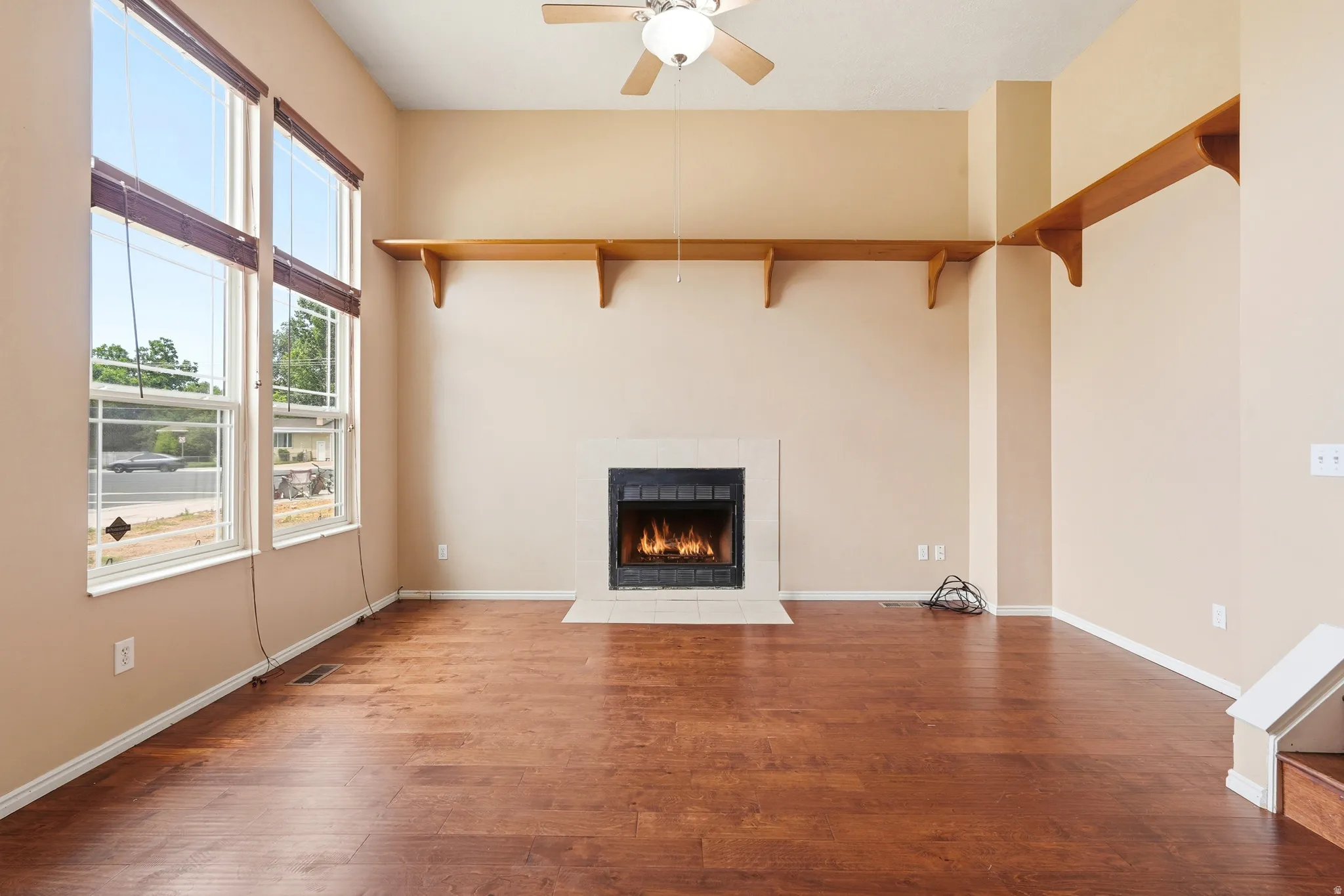 Living area featuring a fireplace with a light-toned surround, high ceilings, large windows, wood-finish flooring, and built-in shelving