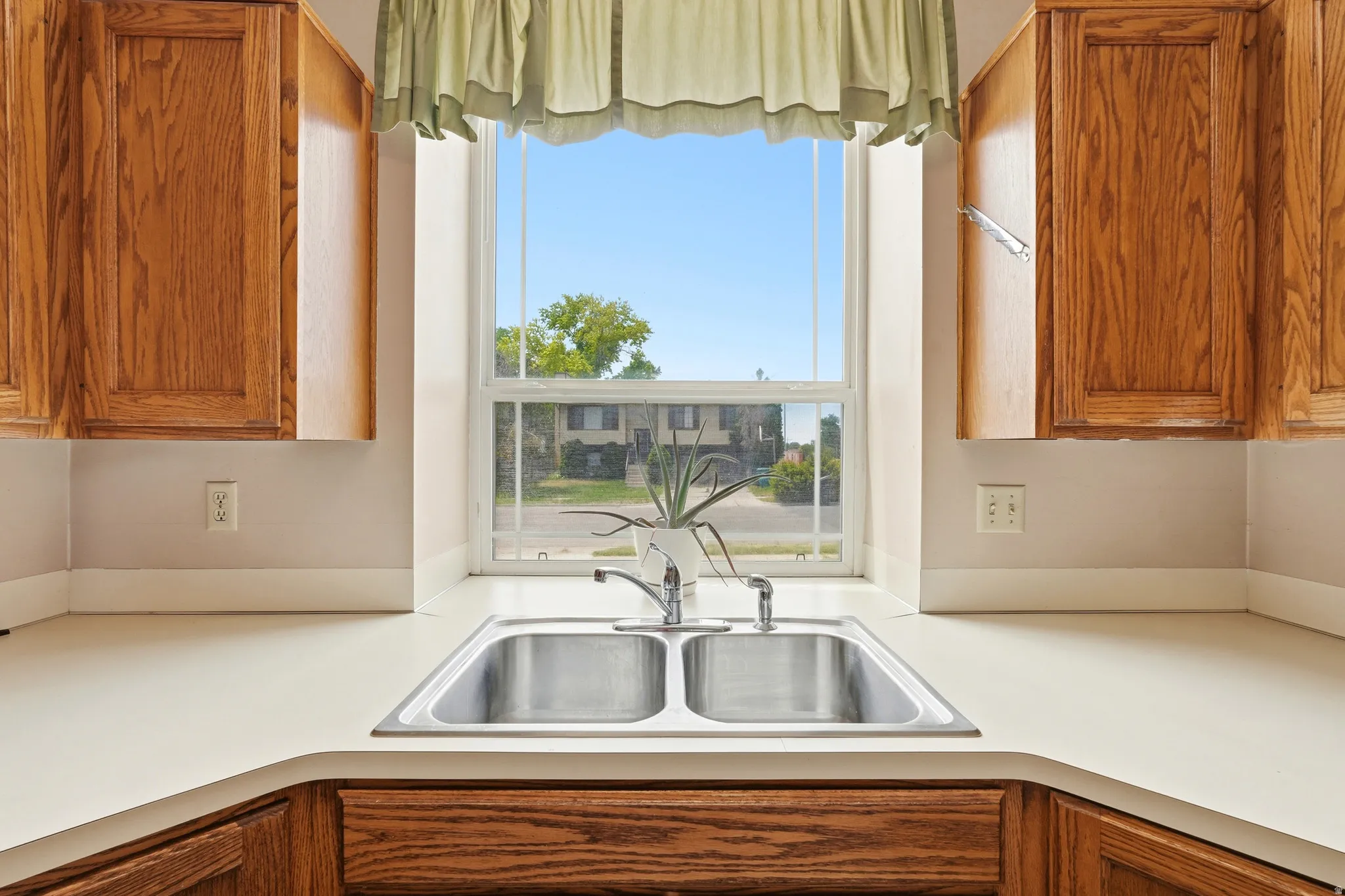Kitchen workstation featuring a double-basin stainless steel sink with a chrome faucet, light-toned countertops, and wood-finish cabinetry