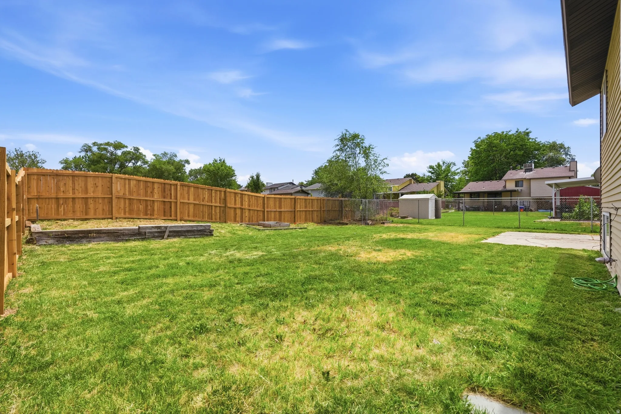 Expansive backyard featuring a large grass area, wood fencing, and concrete patio