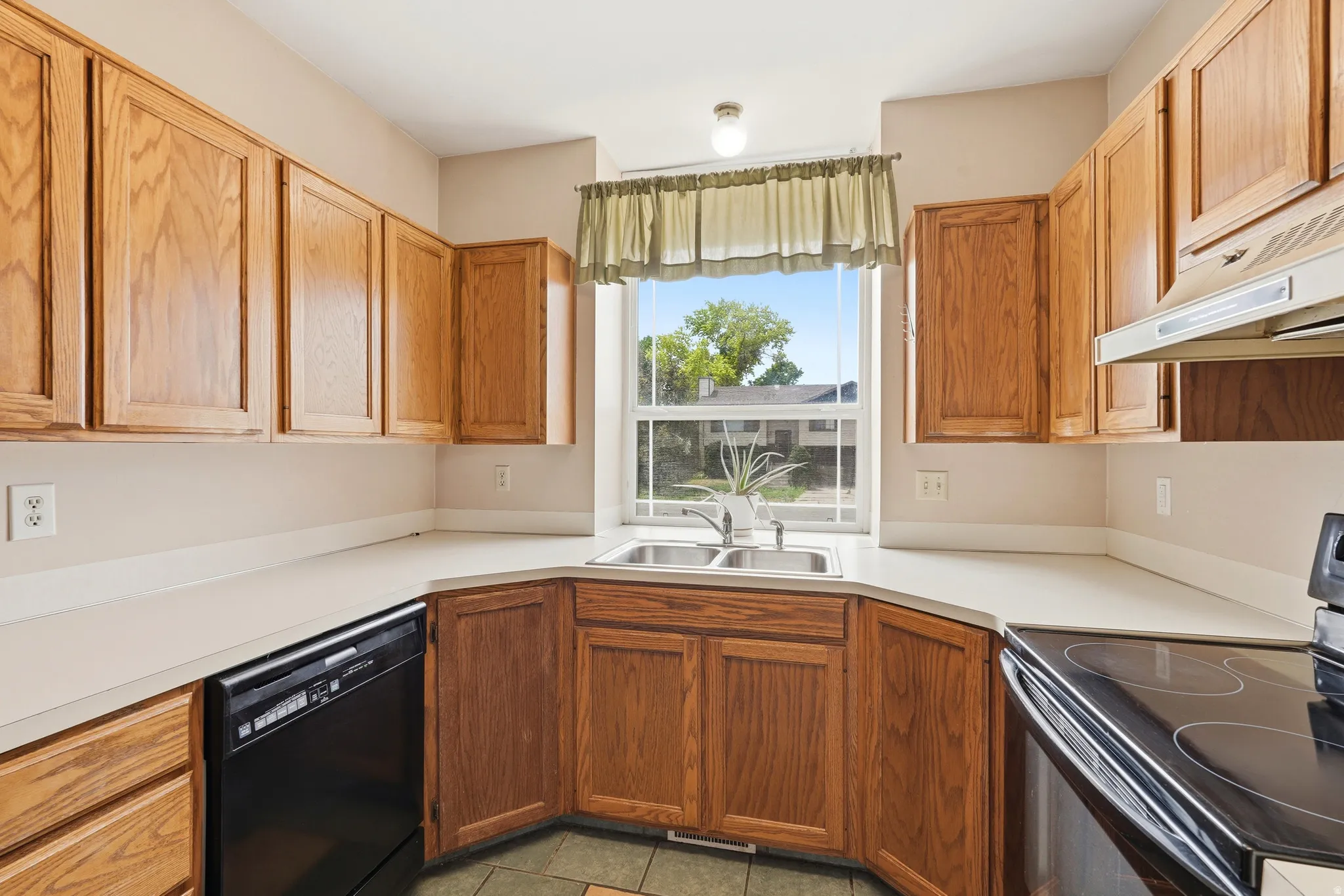 Kitchen featuring wood cabinetry, light-toned countertops, a double basin stainless steel sink, and a black built-in dishwasher