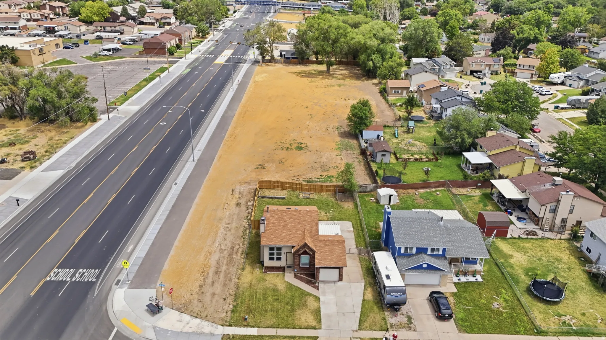 Expansive undeveloped lot featuring direct road frontage, established residential surroundings, and mature trees in the background