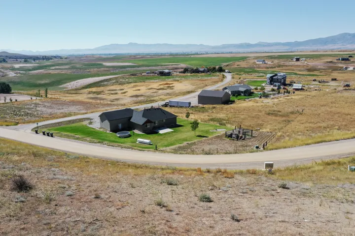 Expansive rural property featuring a primary residence with a dark shingle roof, an attached garage, and a separate large outbuilding