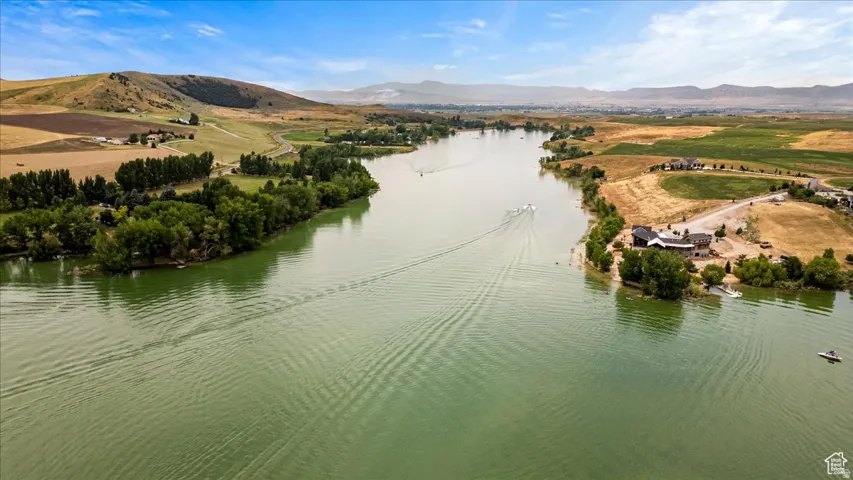 Expansive waterfront property featuring a substantial body of water, natural green foliage, rolling hills, and distant mountains under a clear sky