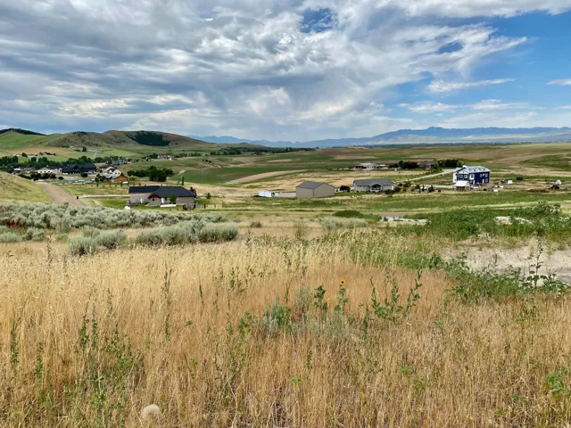 Expansive undeveloped land featuring natural grasses and scattered sagebrush, offering distant mountain ranges and scattered residential structures