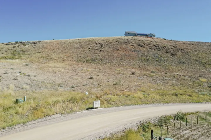 Rolling hills with natural vegetation and a distant residence atop a ridge