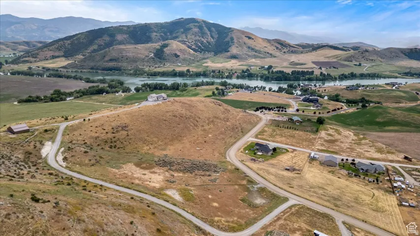 Expansive land parcel featuring paved road access, a distant water body, and mountainous terrain