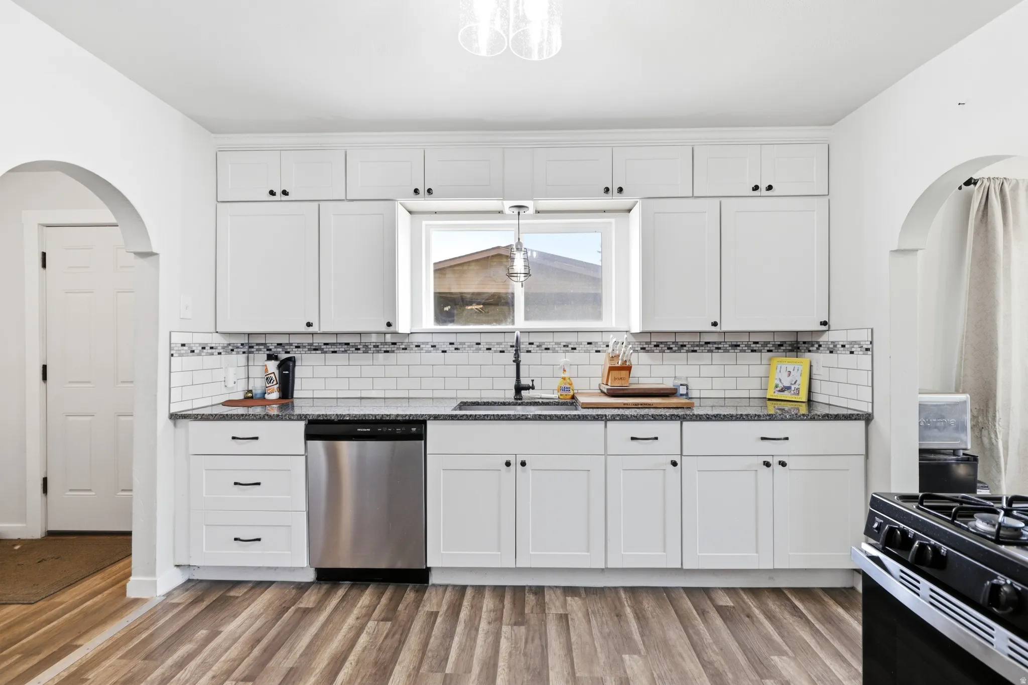 Kitchen featuring white shaker-style cabinetry, granite-finish countertops, subway tile backsplash, and wood-finish flooring