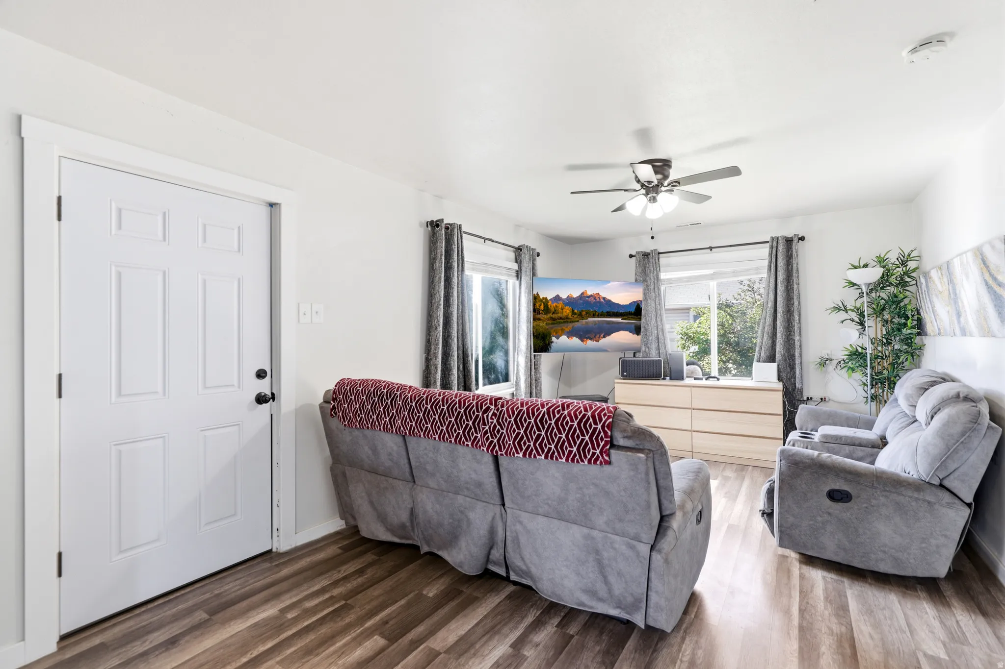 Living area featuring wood-finish flooring, a white six-panel door with black hardware, and light-toned walls
