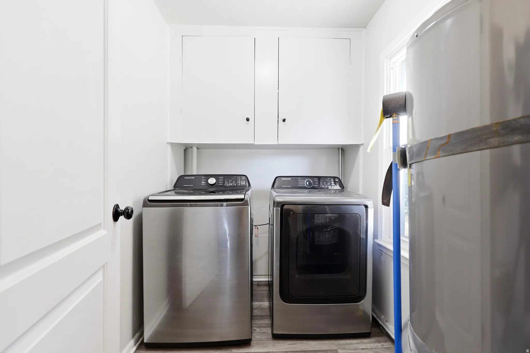 Laundry area featuring overhead white cabinetry and wood-finish flooring
