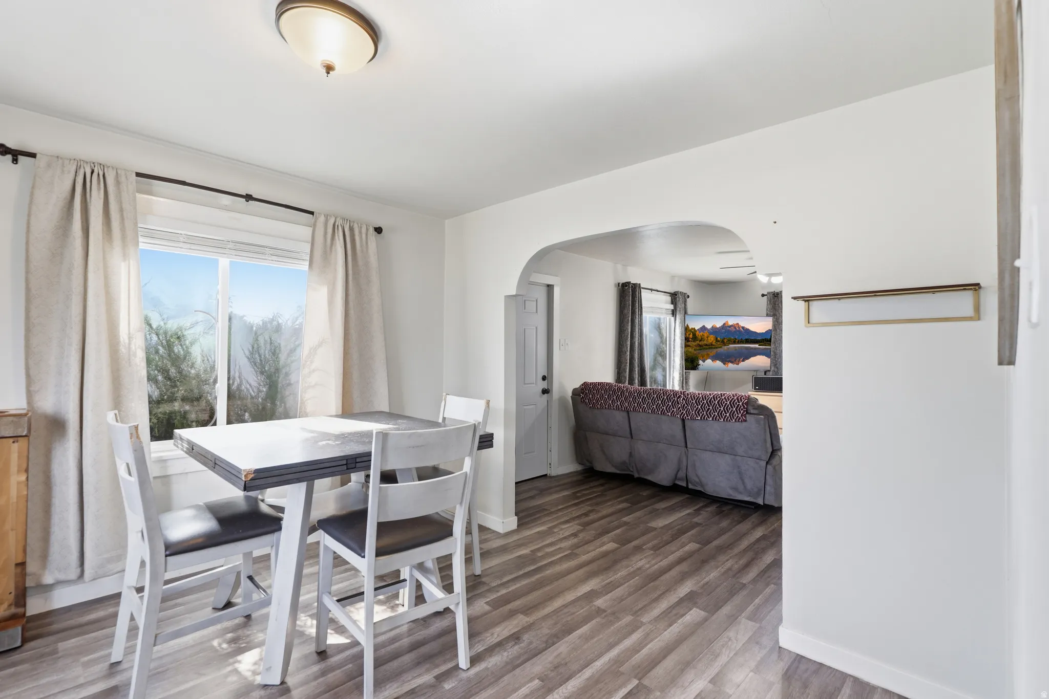 Dining area featuring wood-finish flooring, a window with curtains, and an arched doorway opening to an additional room