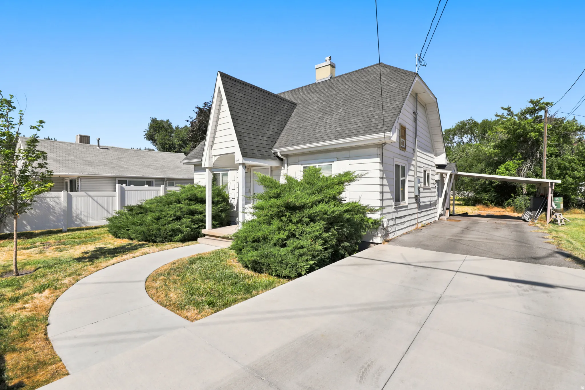 White siding exterior with a prominent gabled roofline, featuring mature shrubbery and a curving concrete walkway