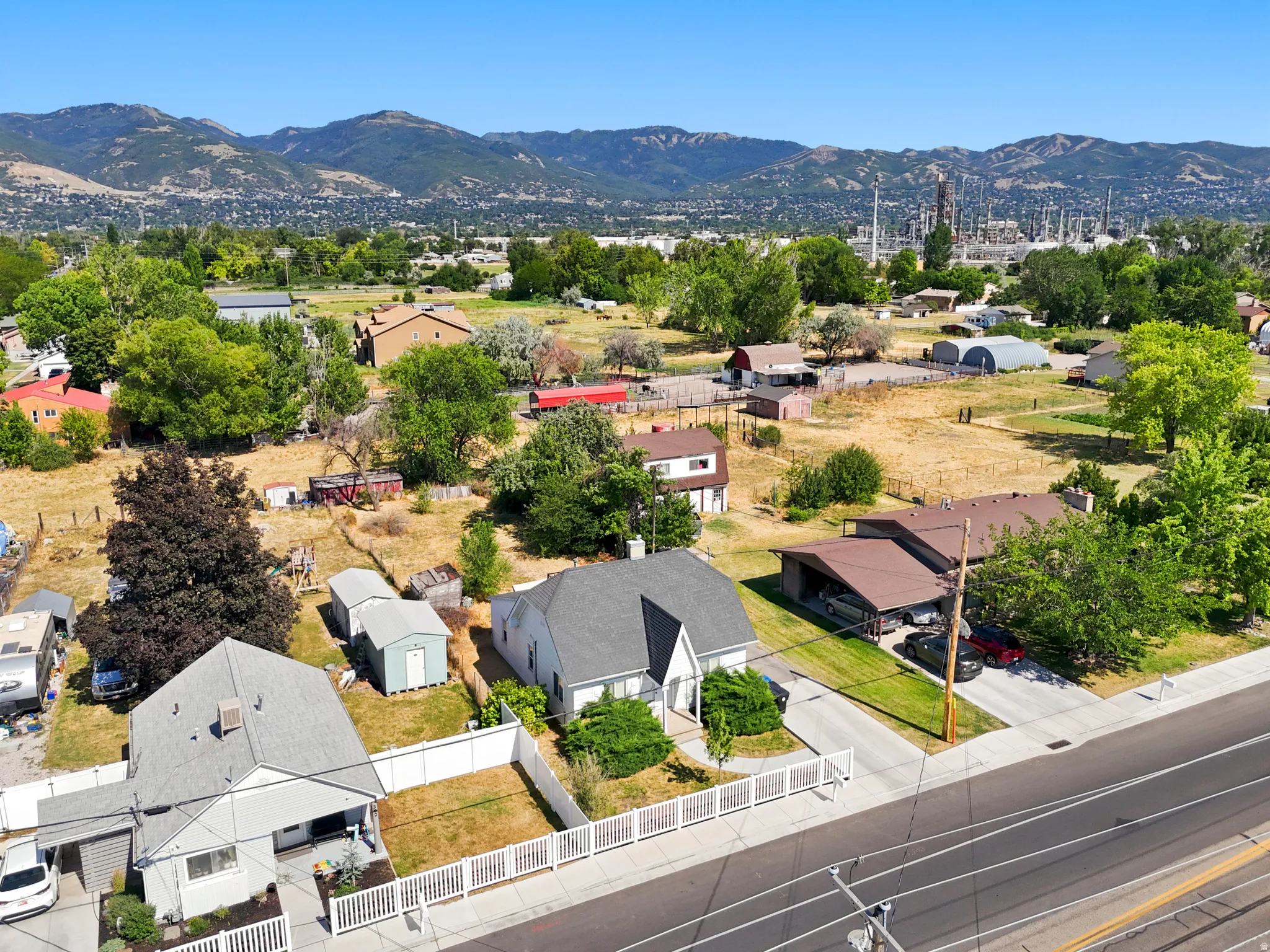 Aerial perspective showcasing a residential property with a gray gabled roof and light-colored siding, featuring a white picket fence enclosing a front yard