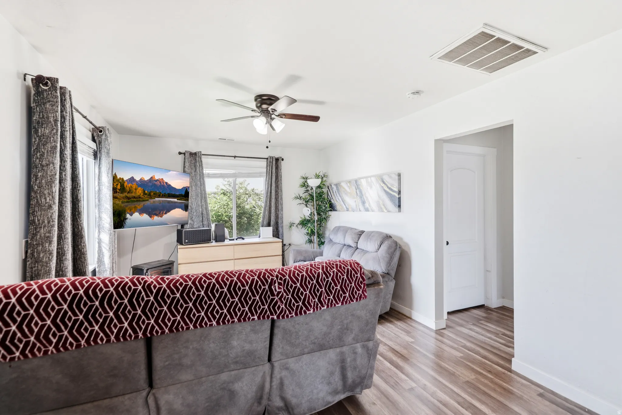 Living area featuring wood-finish flooring, white walls, and a ceiling fan with integrated lighting